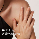 Hand wearing a rose gold ring with text 'Waterproof & Tarnish-Free' on a neutral background