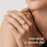Close-up of a hand wearing an emerald-cut diamond ring with text 'Waterproof & Tarnish-free' on a light background.