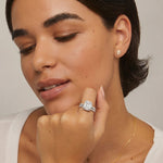 Woman wearing a diamond ring and earrings on a neutral background