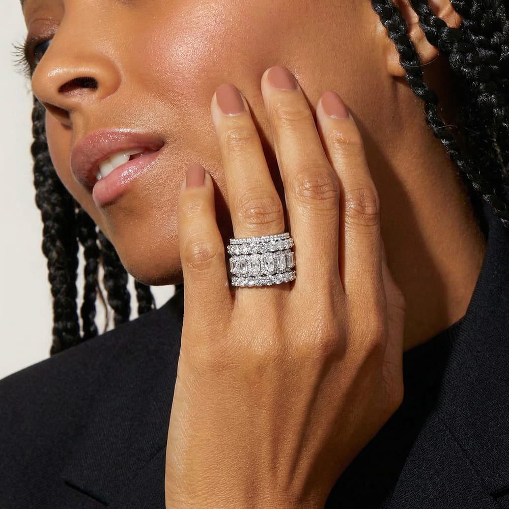 Close-up of a woman's hand wearing a stack of diamond rings, with a neutral background.