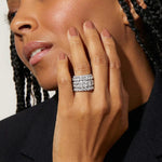 Close-up of a woman's hand wearing a stack of diamond rings, with a neutral background.