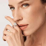 Close-up of a woman's face with two rings on her finger against a neutral background