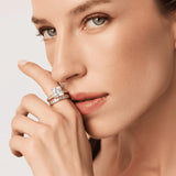 Close-up of a woman's face with two rings on her finger against a neutral background